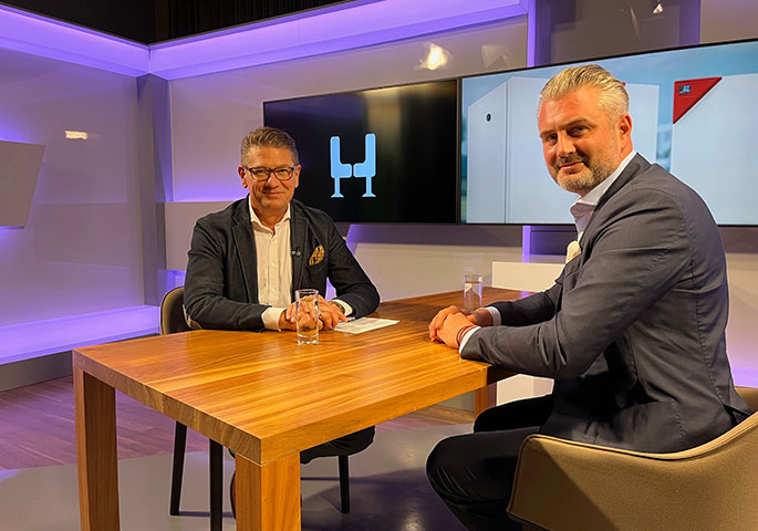 Regio TV presenters Rolf Benzmann and Michael Binder-Pfaff sit opposite each other at a table in the recording studio and look into the camera.