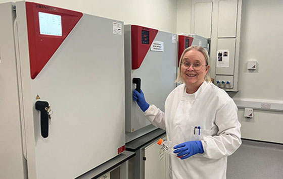 Pilomena Hallford standing in front of BINDER CO2 incubators holding a cell culture flask in her hand.