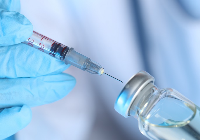 Syringe and vial in a hand wearing a surgical glove.